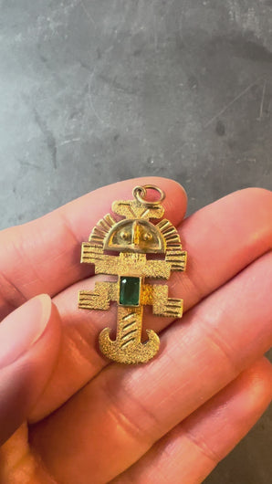 Gold pendant with a green gemstone turned in hand on a grey background